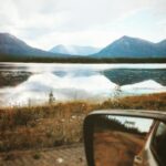 depth photography of car side mirror with a scene of body of water near mountains